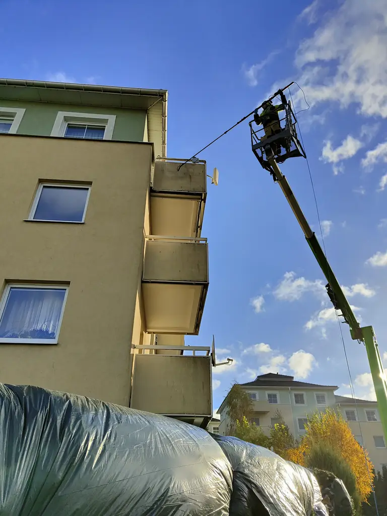 Pracownik czyści elewację i balkon z kosza podnośnika; otoczenie osłonięto folią